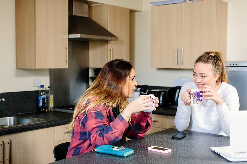Two girls chatting in the kitchen while drinking hot drinks