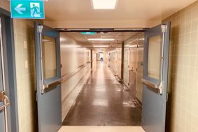 Long, empty hospital corridor with an exit sign pointing to a door on the left