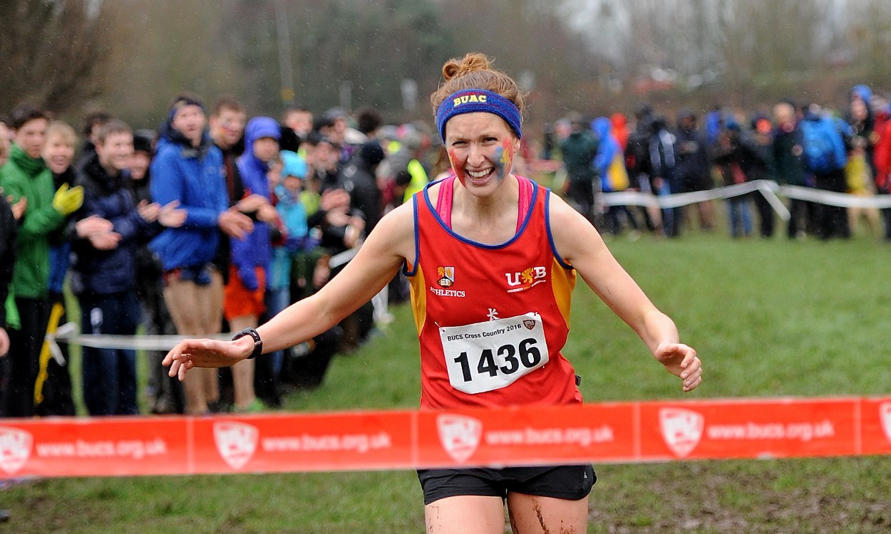 A photo of Pippa Wolven, she is smiling as she approaches the finish line of a cross country race she has just ran.