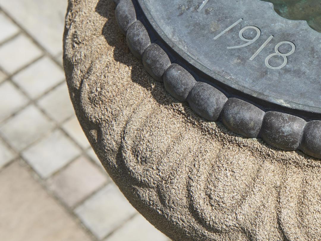 Close up detail from above of stone birdbath with ornate lead inner bowl featuring stone carving around edge