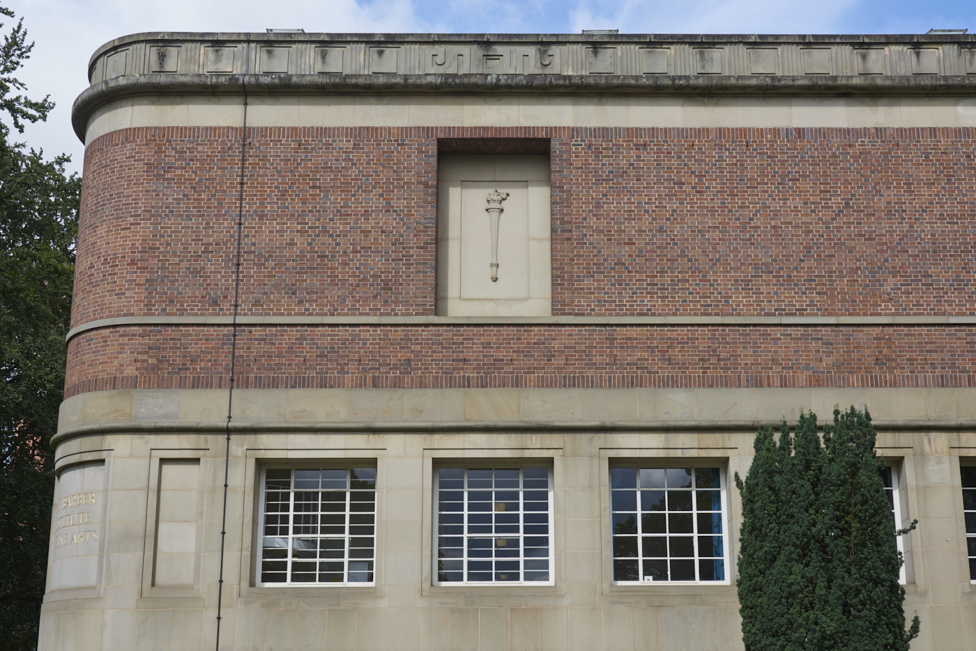 Carved stone panel set into the wall of the Barber Institute of Fine Arts by Gordon Herickx featuring a carving of a torch in context of building