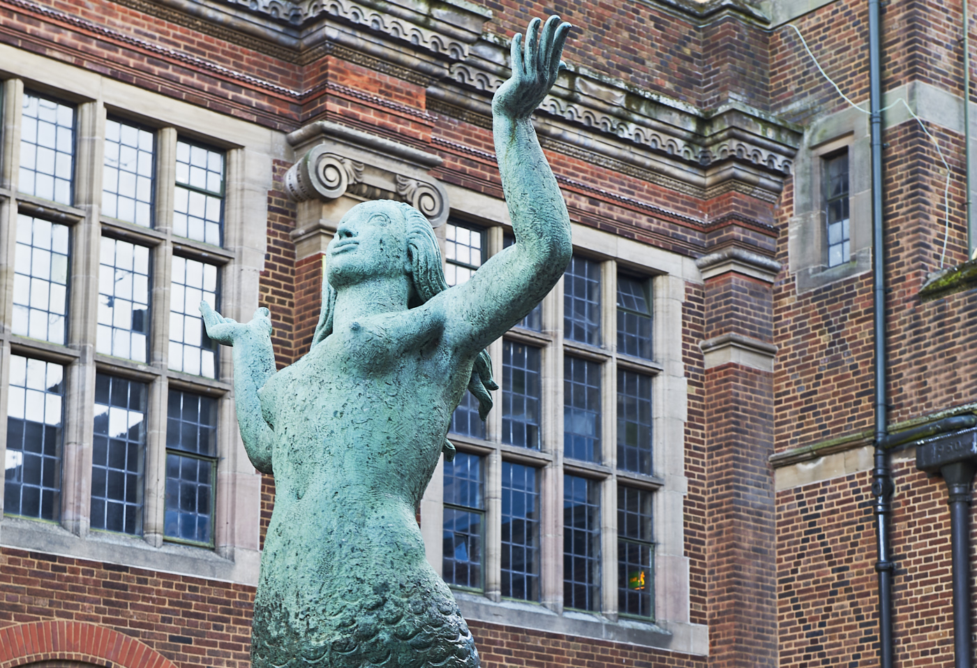 Torso, arms and head in profile of Mermaid Fountain bronze sculpture by William Bloye with Guild of Students behind