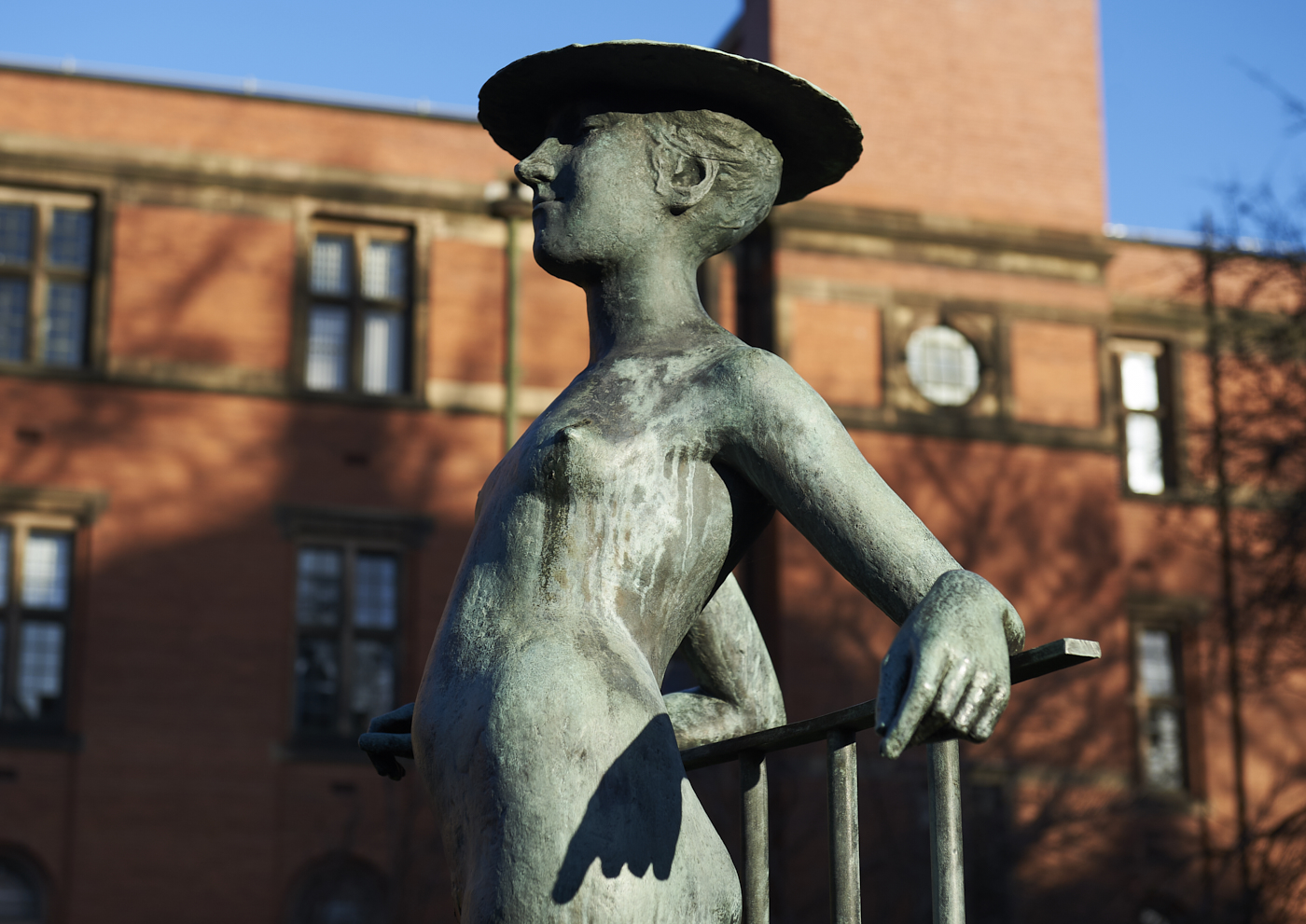 Upper torso in profile of Girl in a Hat bronze sculpture by Bernard Sindall with Law Building behind