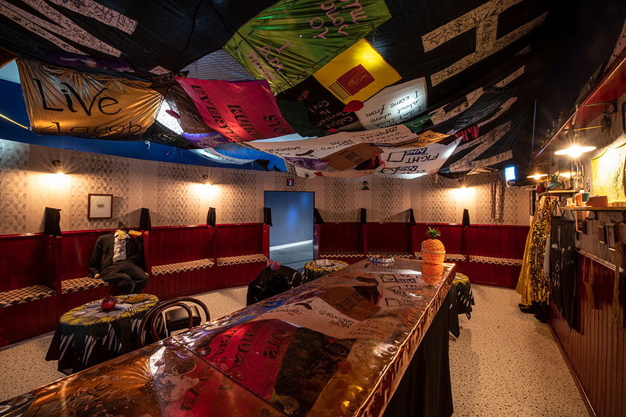 Photograph of art installation in which gallery interior has been set up to resemble a traditional Irish pub. A number of fabric banners hang from the ceiling.