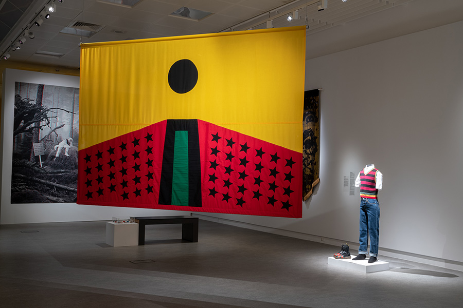 A large yellow, red, and black flag hangs in the centre of a gallery space