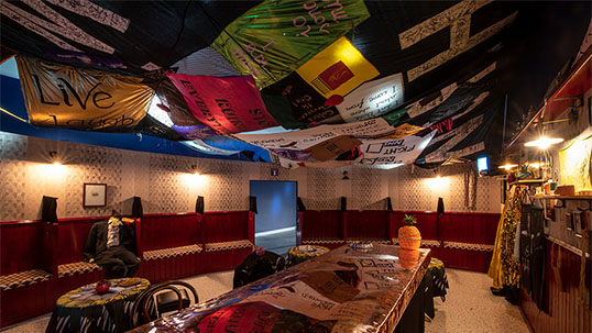 Photograph of art installation in which gallery interior has been set up to resemble a traditional Irish pub. A number of fabric banners hang from the ceiling.