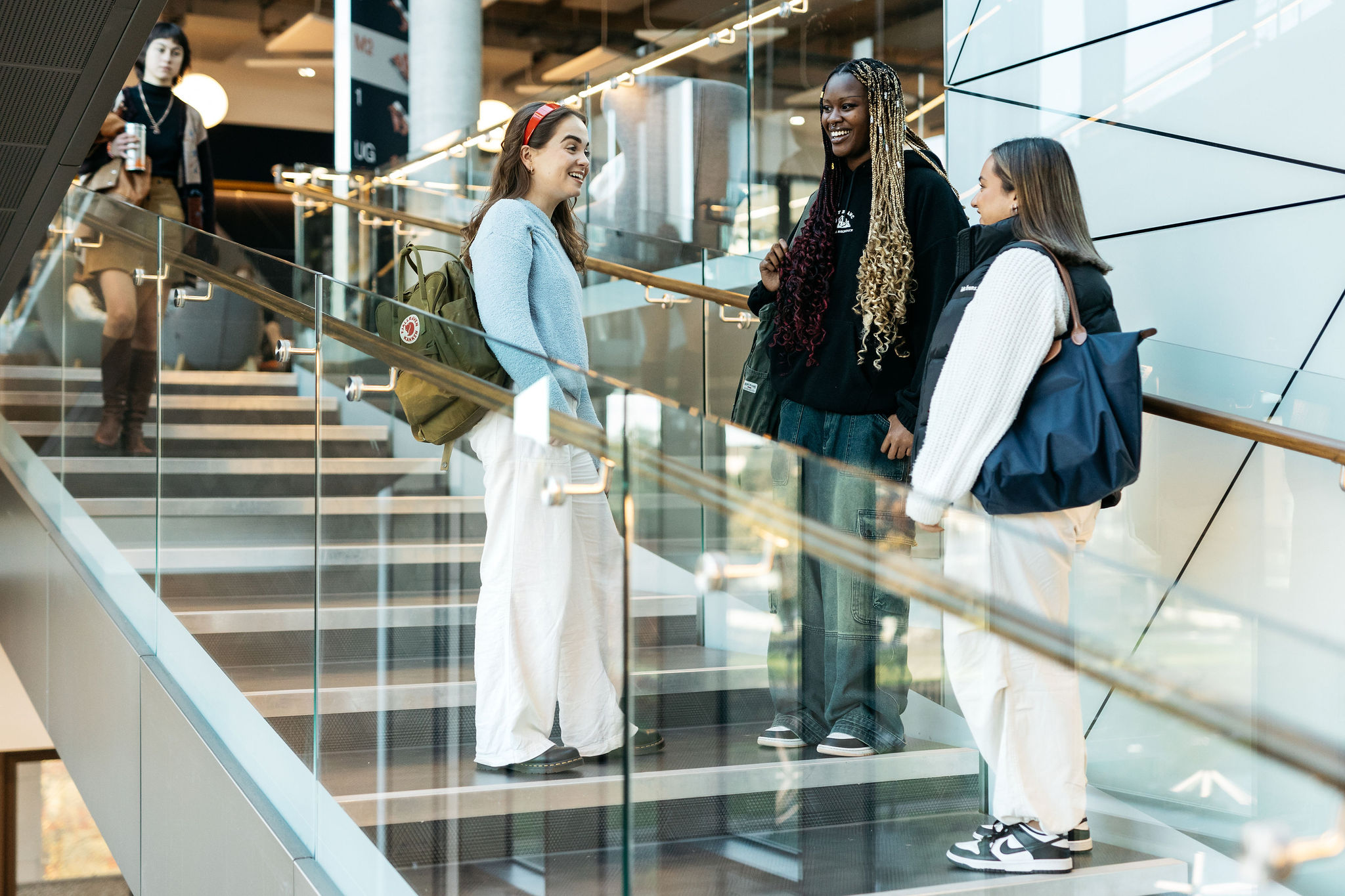 A group of students chat and laugh while descending a staircase