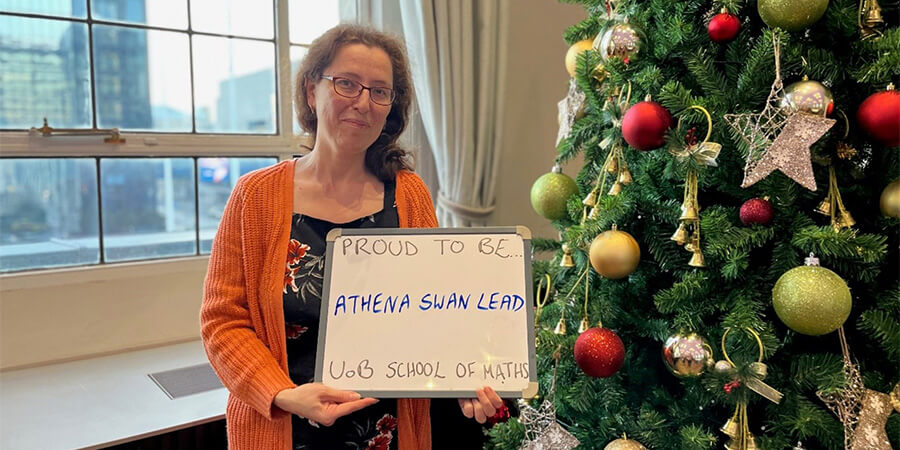 Professor Olga Maleva holding sign "proud to be Athena Swan lead, UoB School of Maths"