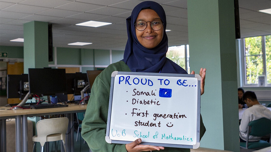 Rahma Abdulahi holding a sign saying Proud to be Somali, Diabetic, First-generation student, UoB School of Mathematics