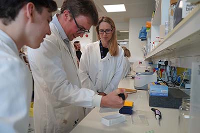 Professor Alex Sinclair with members of IIH UK in a lab with a member using a pipette