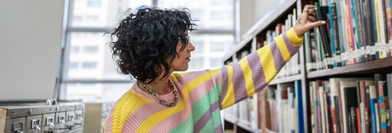 Woman reaching out for book on bookshelf