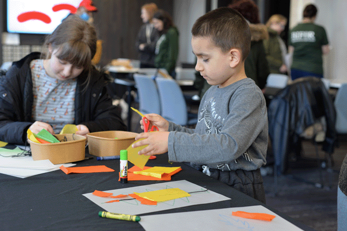 Two young children having fun doing arts and crafts at a table covered in coloured paper, glue, scissors and other crafting items
