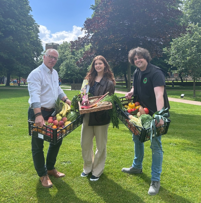 Olivia Eaton standing with two other people on campus holding boxes of fresh fruit and vegetables