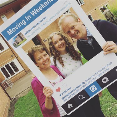 A mother and father with their daughter, holding up an life-sized Instagram frame on moving in day