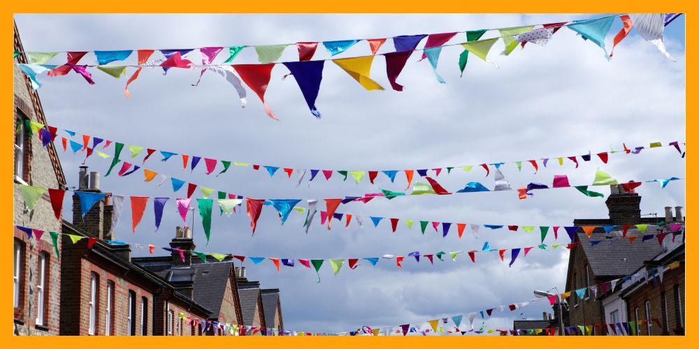 Multicoloured triangle bunting sways in the wind, stretched in the sky from home to home on a street.