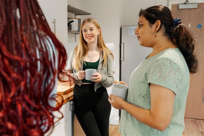 Three students in their house drinking tea and coffee