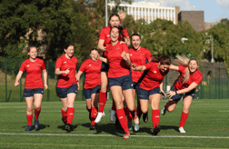 A women's hockey team celebrating on a hockey pitch