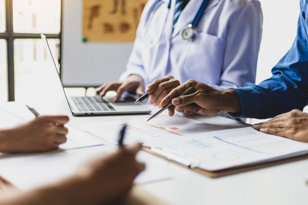 Doctors consult a chart with pens and a laptop.