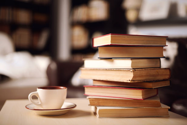 A stack of books sits on a table next to a cup of coffee in a library cafe setting.