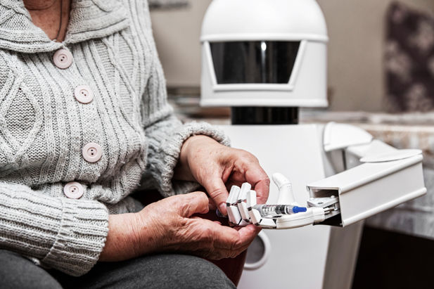 An elderly woman placing a syringe into the open palm of a small white robot.