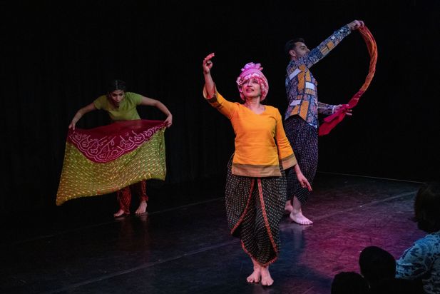 Three South Asian women smile with their arms crossed dressed in brightly coloured traditional celebratory dress.