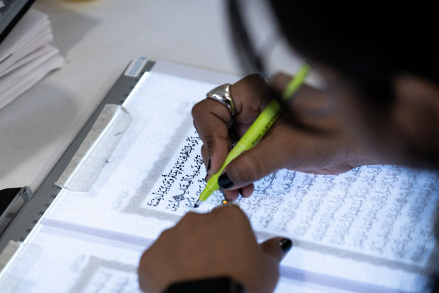 An over the shoulder view of a woman tracing a passge from the Qu'ran.