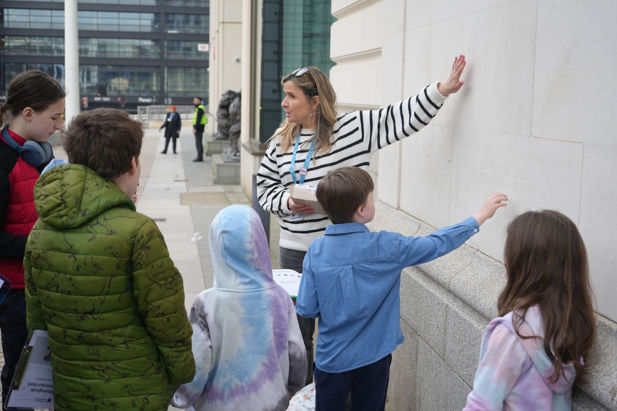 A woman encourages a young tour group to touch the exterior of The Exchange.