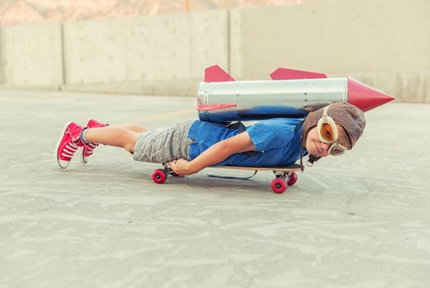 A boy with a rocket on his back lies on a skateboard