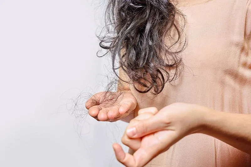 Woman holding a clump of black hair that has come away from head