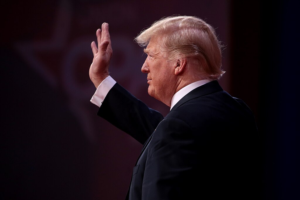 Donald Trump facing the left waving to a crowd off camera.