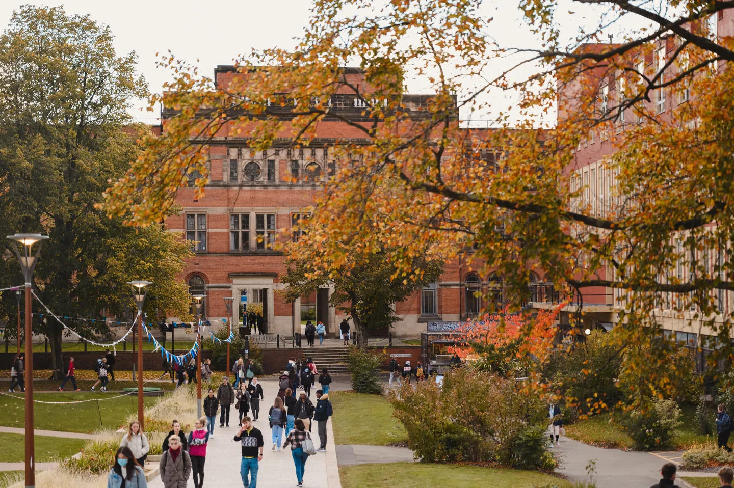 University of Birmingham campus - group of people walking through green space. Red brick large building to the rear