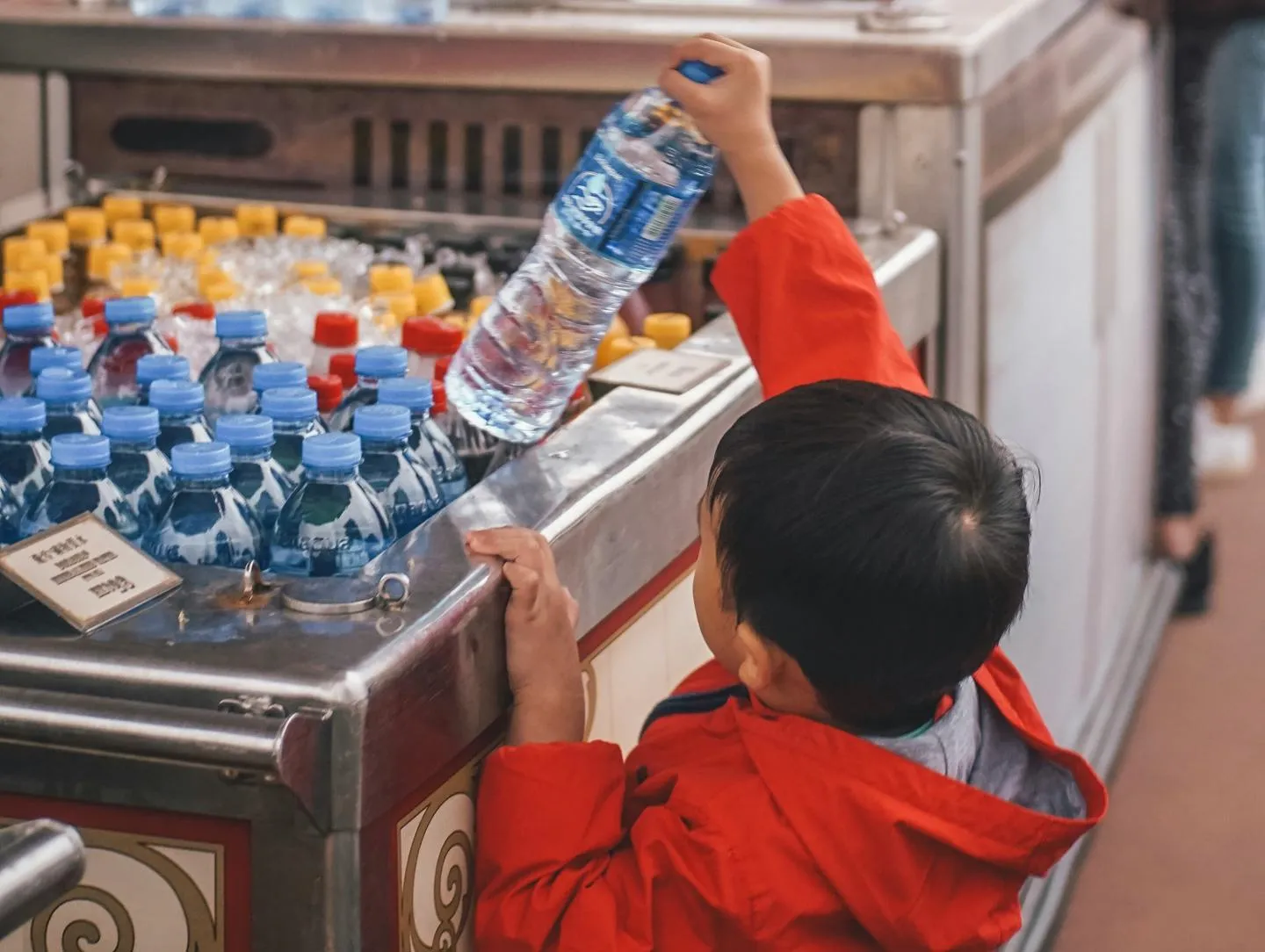 A small boy reaching for a bottle of water in a shop