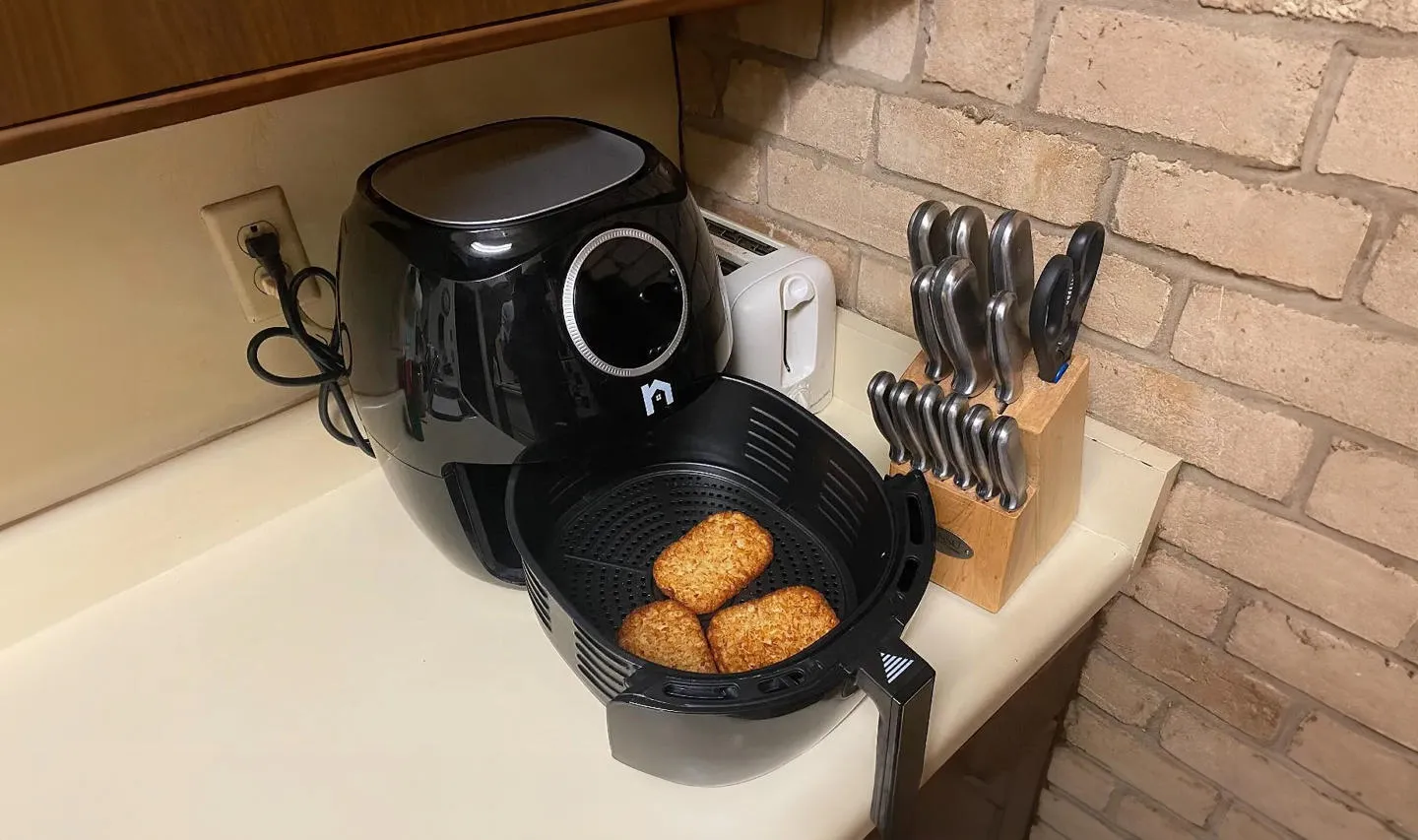 An air fryer on a kitchen counter with some hash browns in the basket