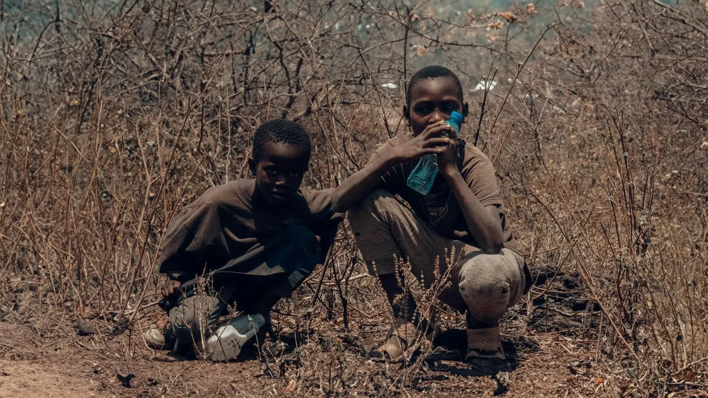 Two African boys crouching in arid undergrowth