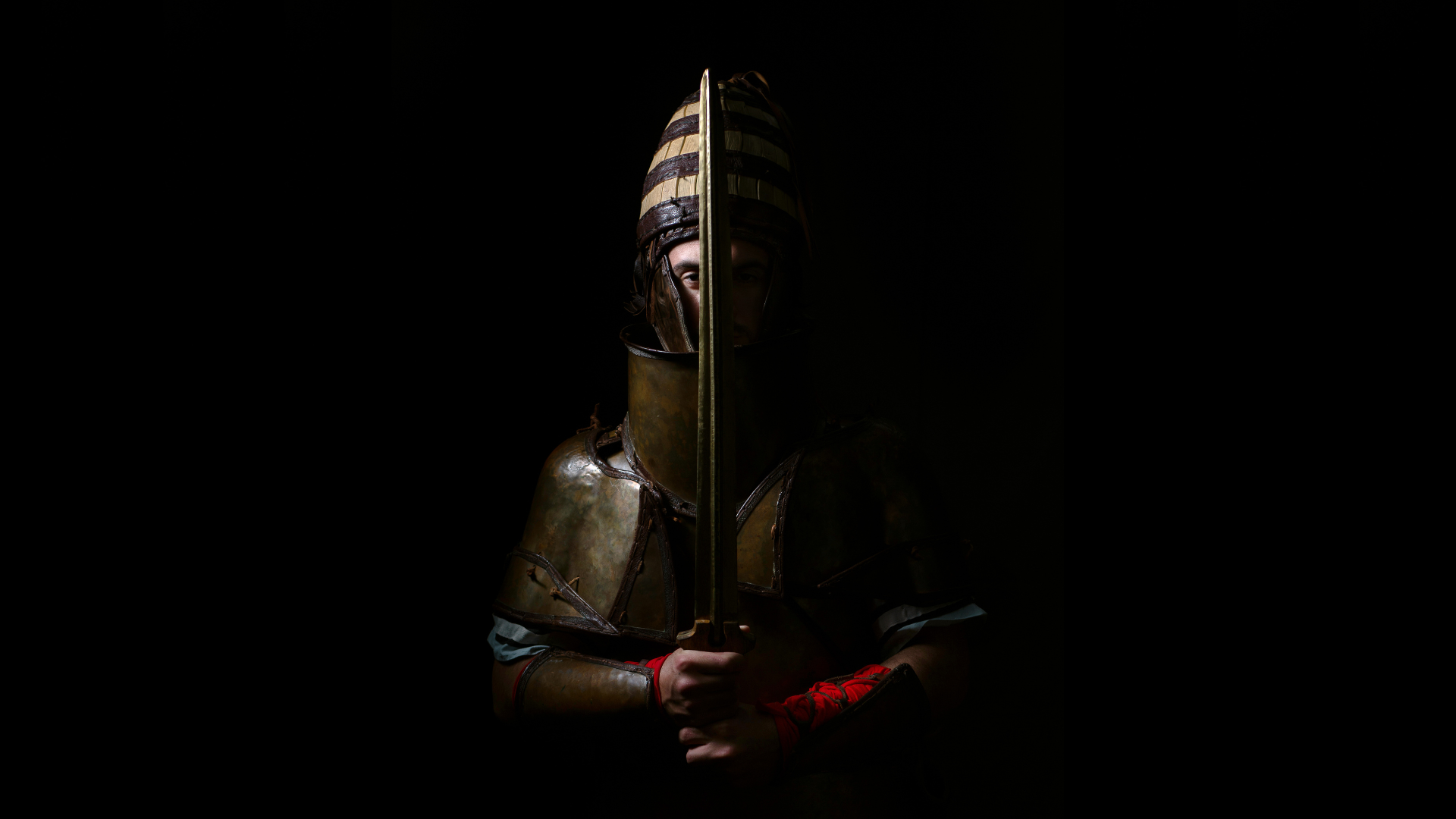 A man wearing the replica armour and holding a sword against a black background