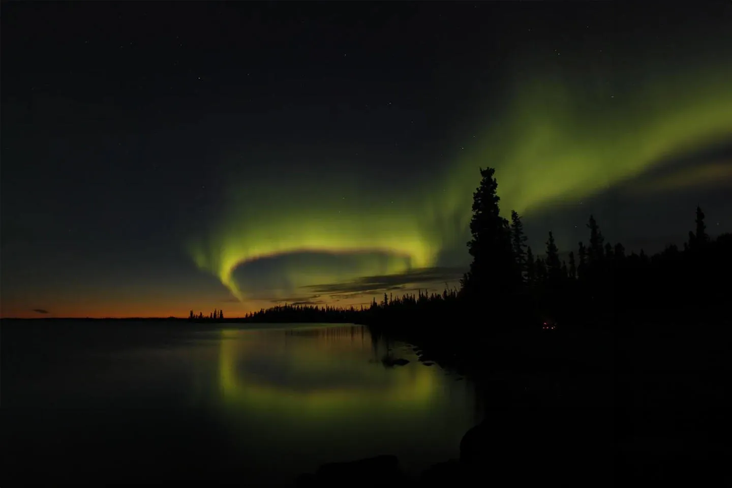 Yellow-green aurora borealis reflected on the shoreline of a still lake 