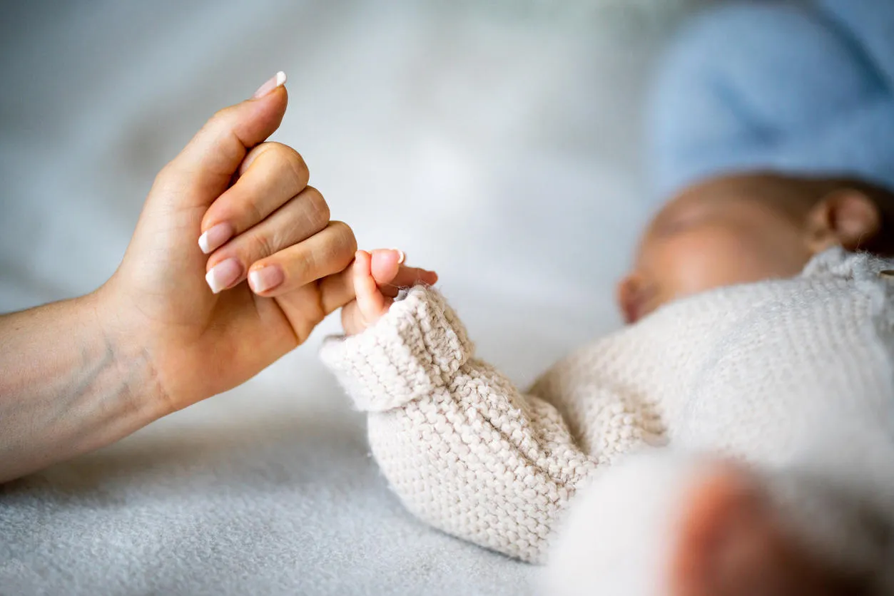 A baby holds a woman's little finger. 