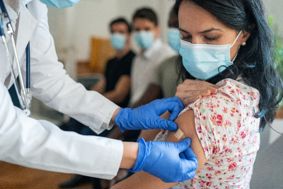Patient wearing a mask is given a plaster following a vaccination by doctor in white coat wearing gloves