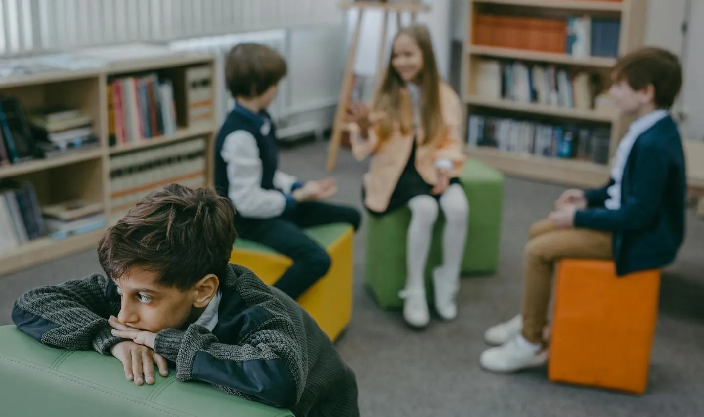 Sad-looking boy being ignored by laughing group of schoolchildren