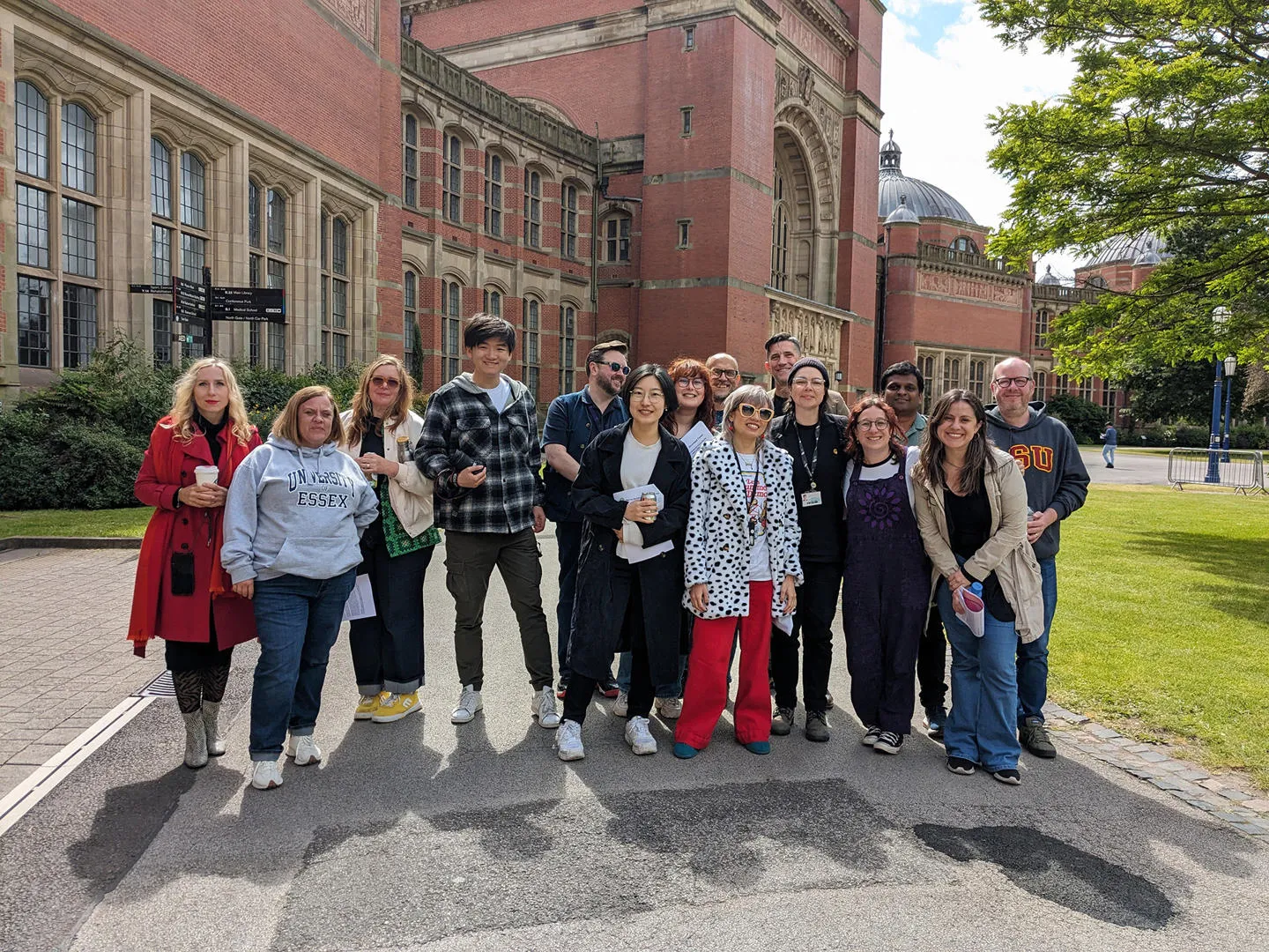 A group of postgraduate students lined up for a group photo in front of the University of Birmingham's redbrick buildings