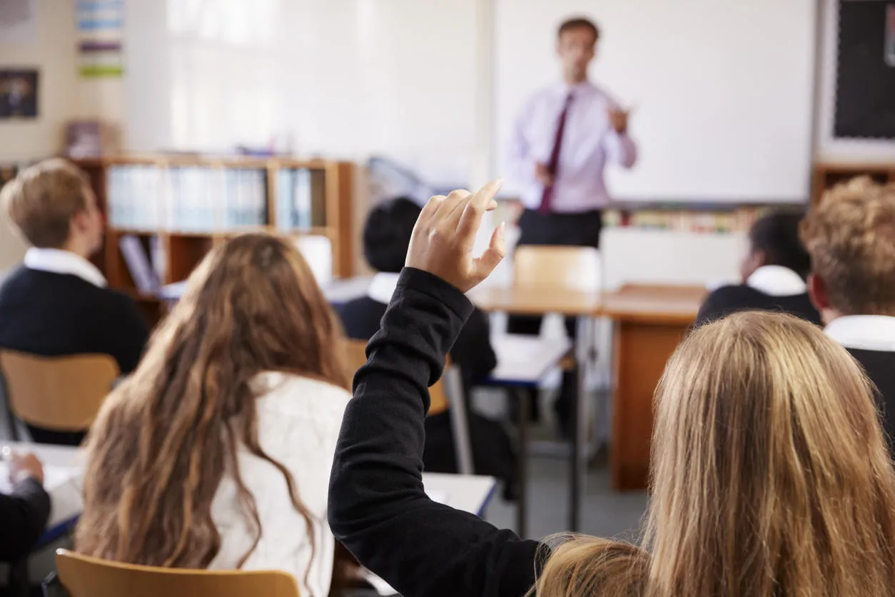 Female student raising her hand to ask her teacher a question. 