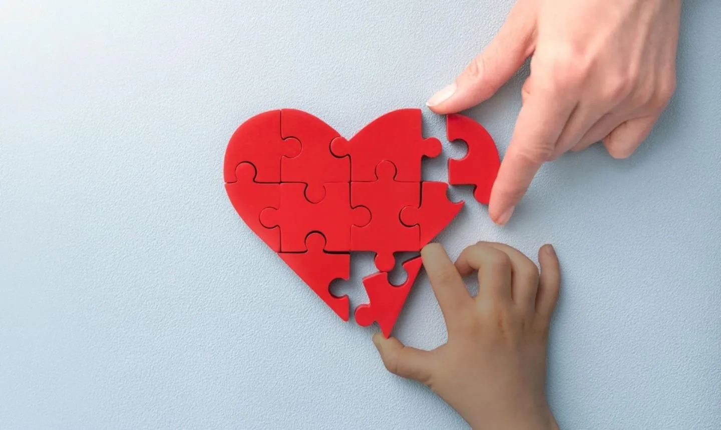 Jigsaw puzzle of a heart with two hands putting pieces into nearly completed puzzle