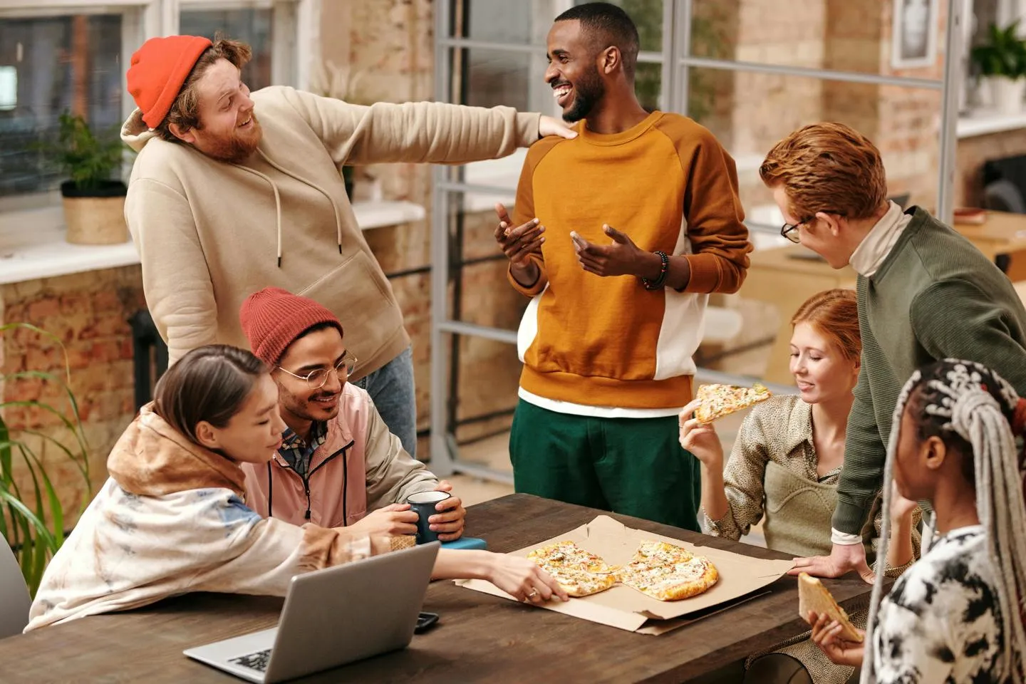 A diverse group of friends enjoy talking to each other over pizza