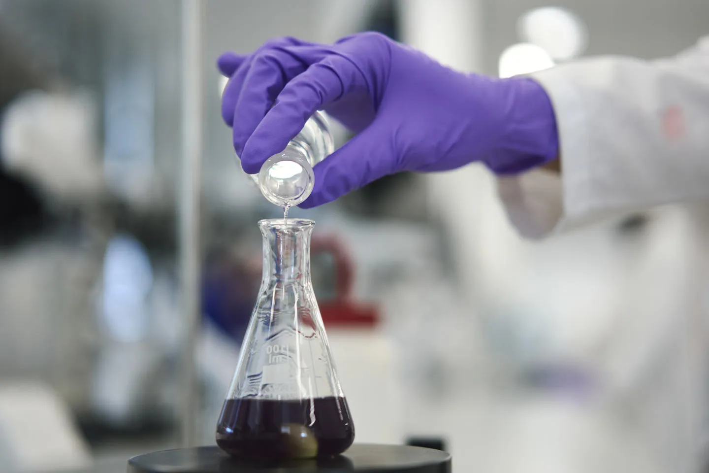 Gloved hand pours liquid into lab flask