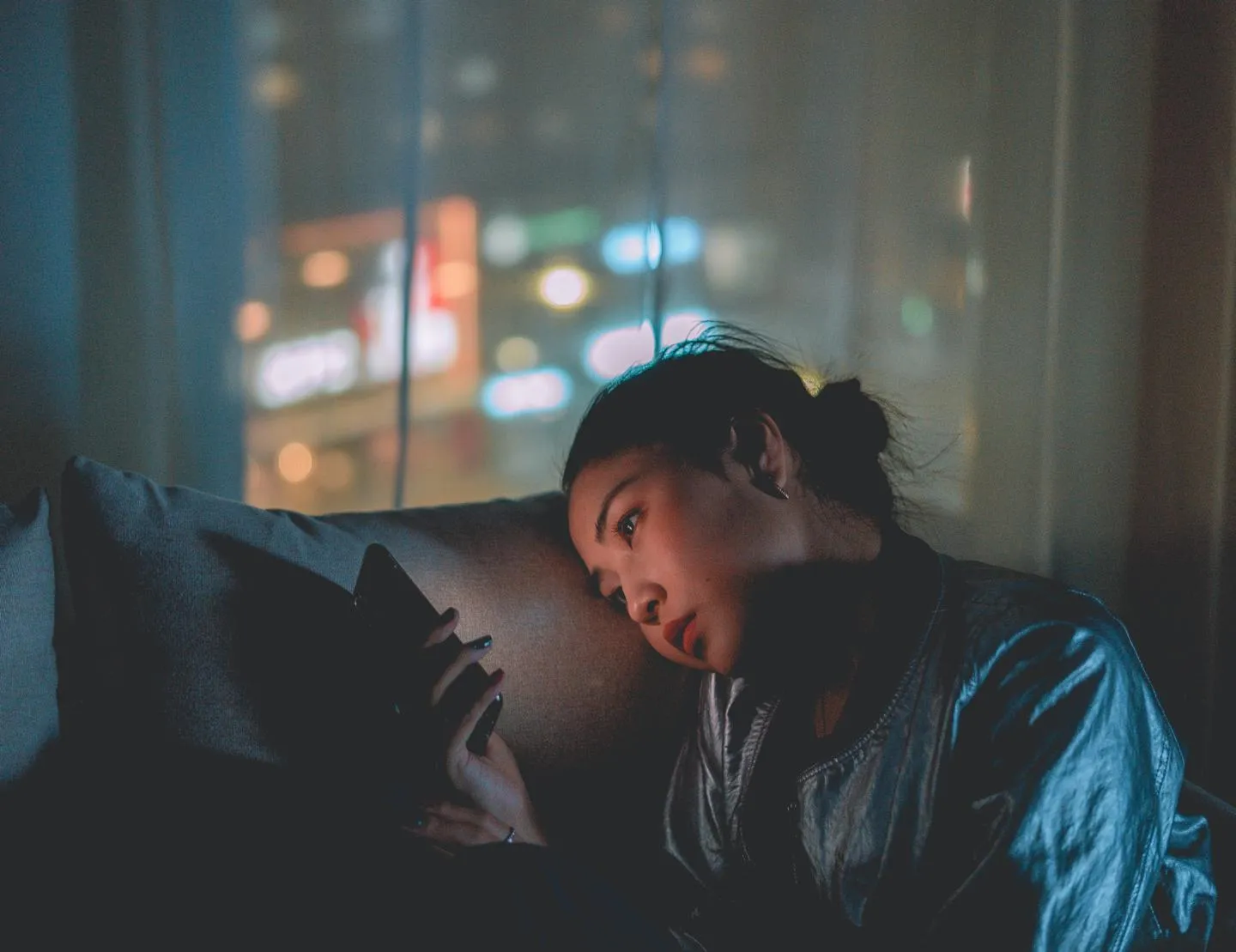 Young woman looking at her phone whilst sitting on a sofa in the dark.