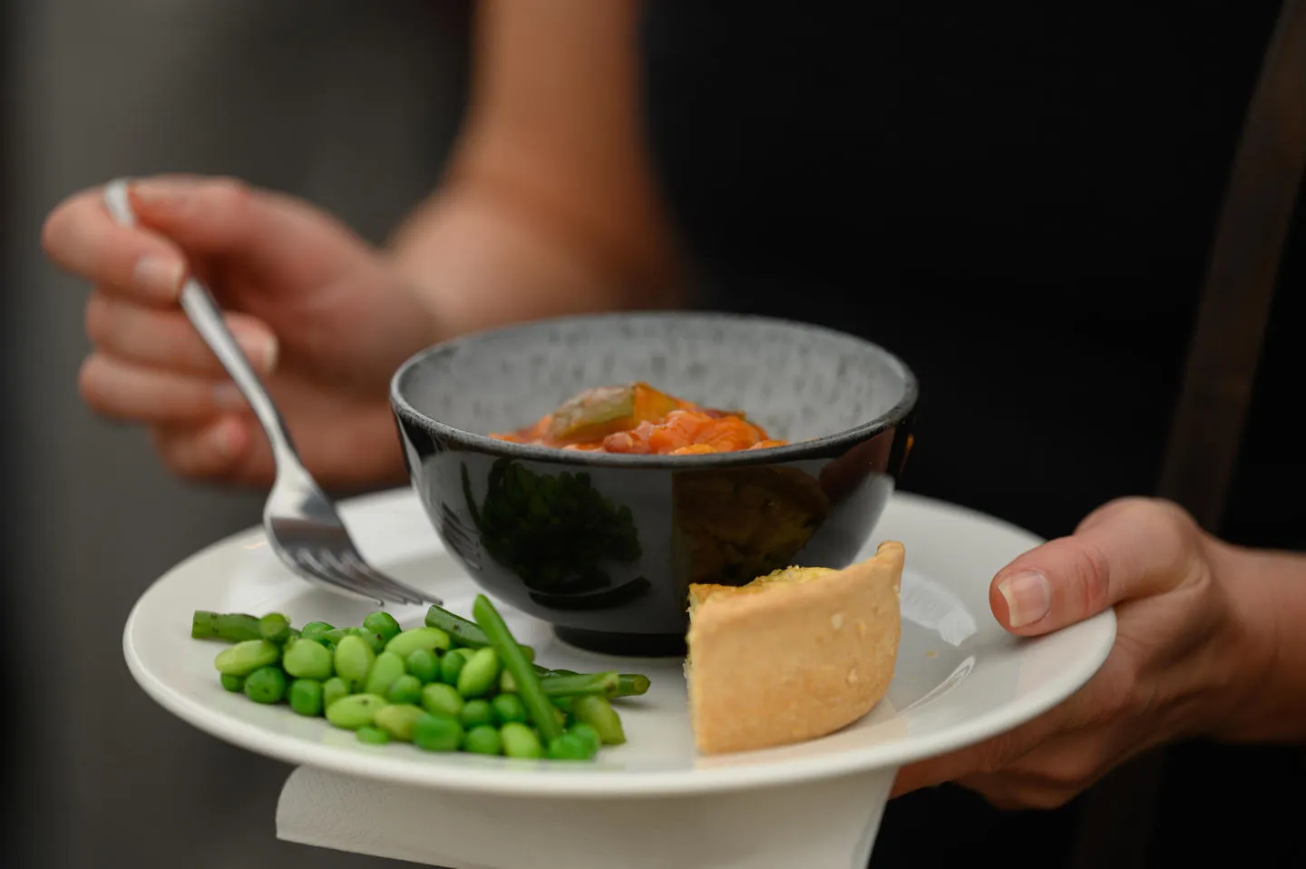 A woman holding a plate of food including green vegetables