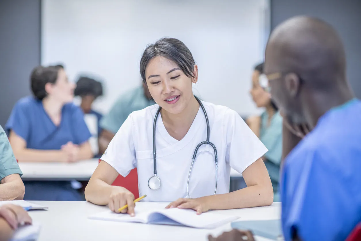 Healthcare professional with stethoscope looking at a notebook in a training session with colleagues