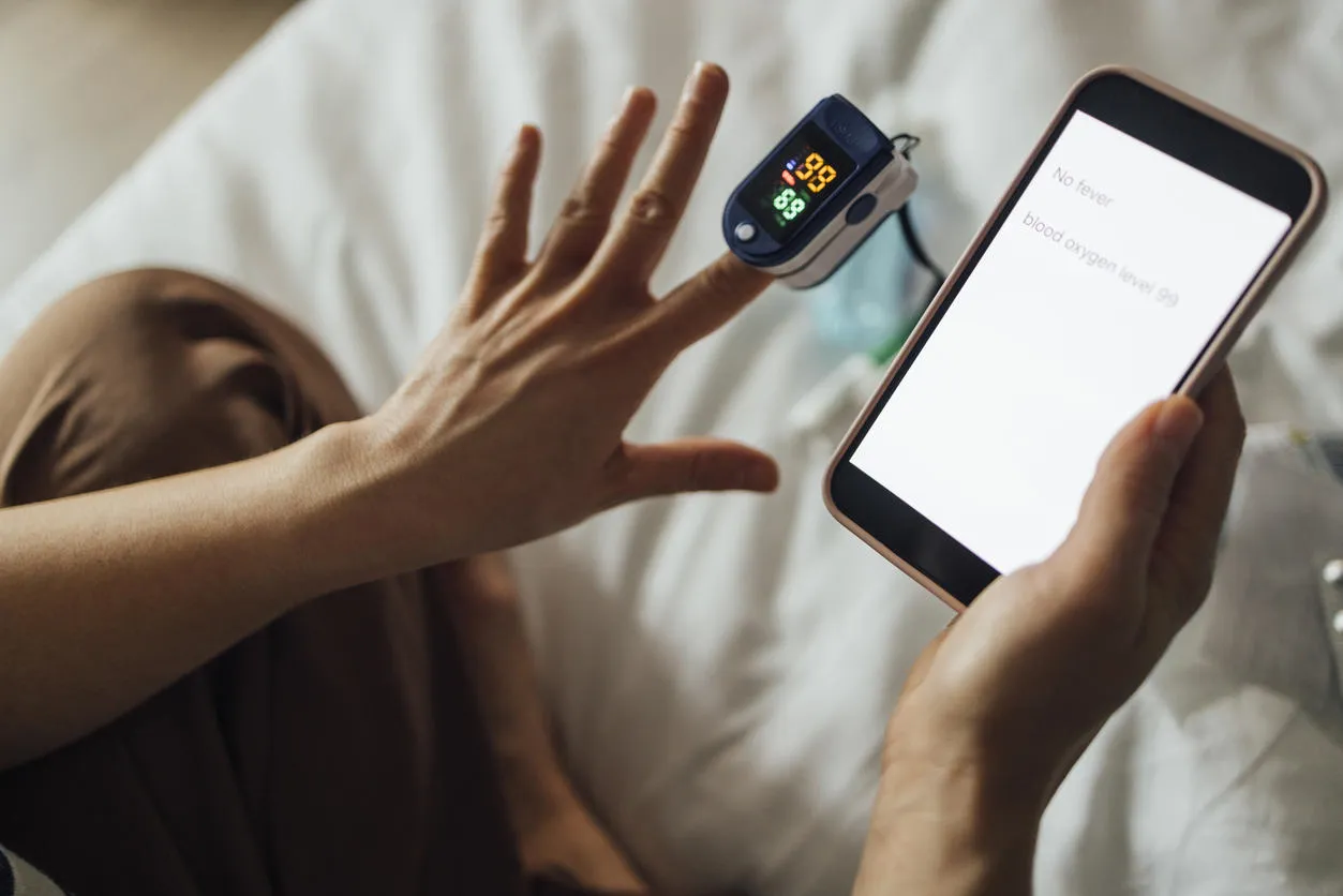 Woman using oximeter to check her blood condition and sending the report to her doctor using a mobile phone.