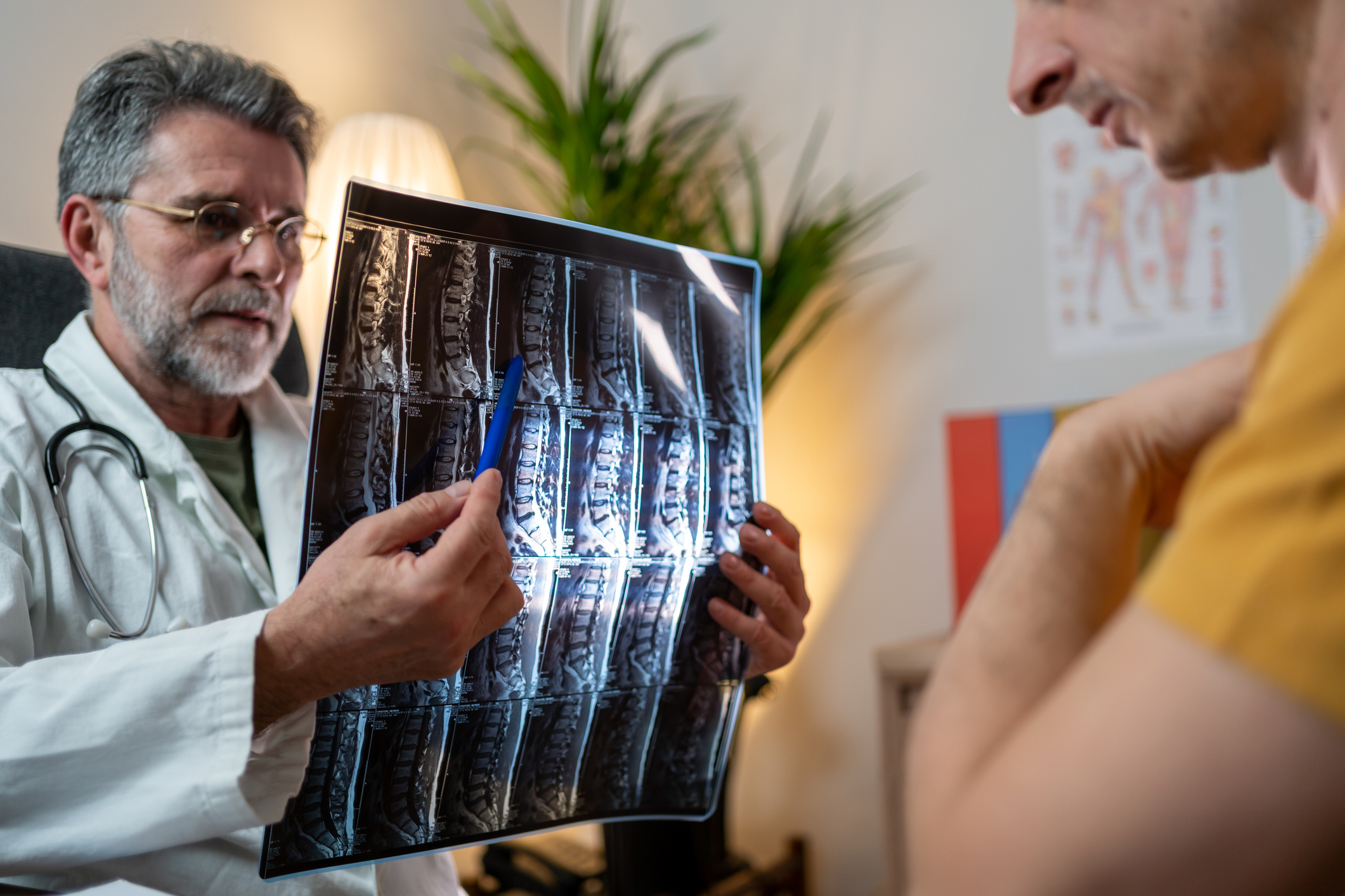 A doctor talking with patient, using a pen to point at a spinal cord scan
