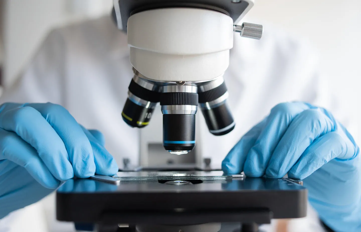 Researcher working with a microscope in a laboratory wearing blue gloves.